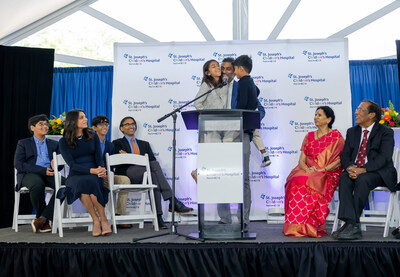 Tampa business leader and philanthropist Sidd Pagidipati holds his children, Aria and Aren, while announcing a transformative $50 million donation to honor his parents’ legacy as health care providers, their 50th wedding anniversary and their 50th anniversary of coming to the United States. Pictured left to right: Ishan, Ami Pagidipati, Arjun, Rahul Pagidipati, Aria, Sidd Pagidipati, Aren, Dr. Rudrama Pagidipati, Dr. Devaiah Pagidipati and Srujani Pagidipati.
